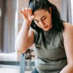 Overweight woman with dark hair in sportswear wiping sweat from face while training in gym in daytime