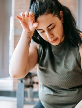 Overweight woman with dark hair in sportswear wiping sweat from face while training in gym in daytime