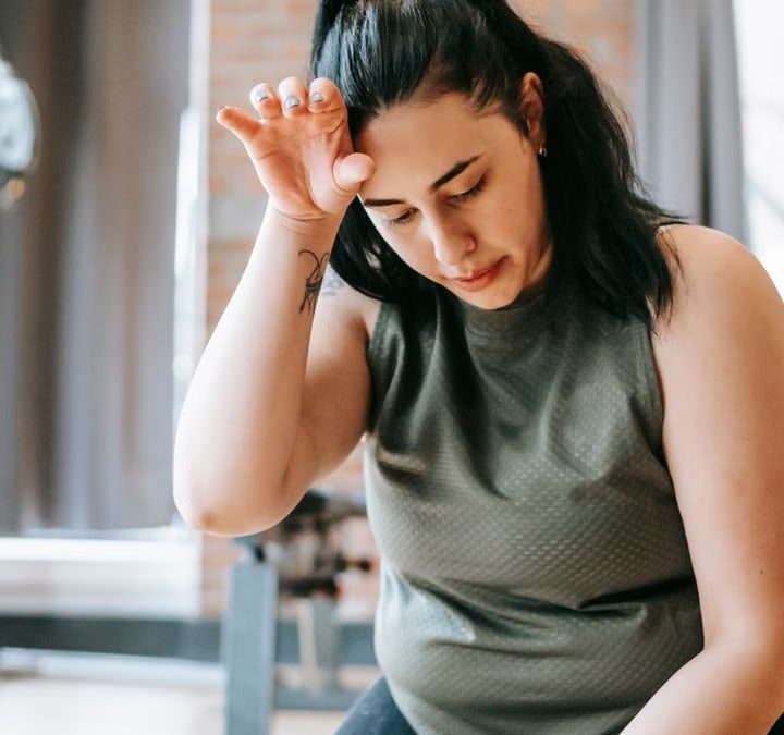 Overweight woman with dark hair in sportswear wiping sweat from face while training in gym in daytime